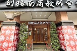 The entrance of a hotel with a traditional Chinese architectural style, featuring a wooden door and red floral patterns on the walls.