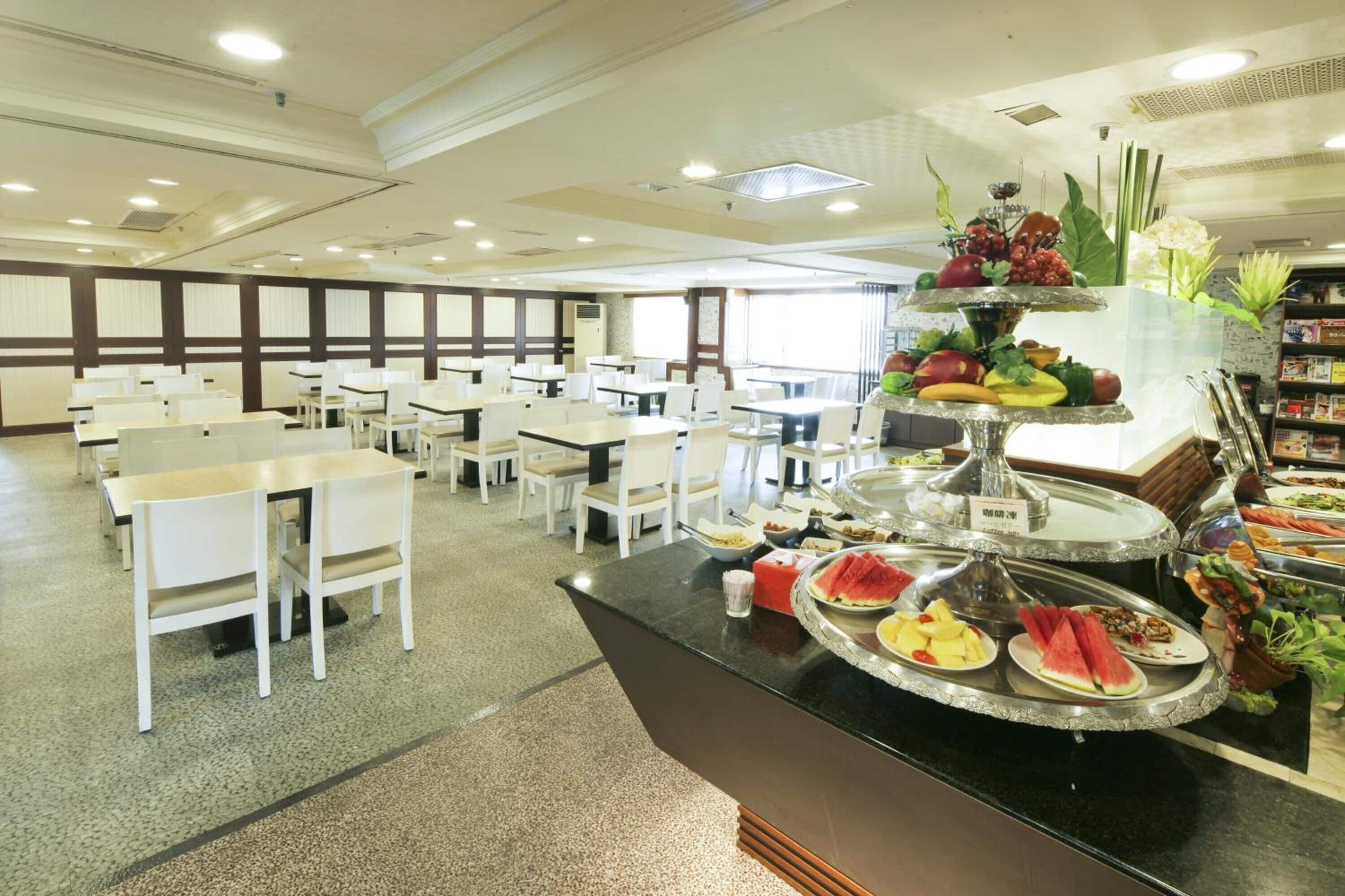 Uma área de buffet com várias estações de serviço, mesas e cadeiras dispostas num espaço amplo.