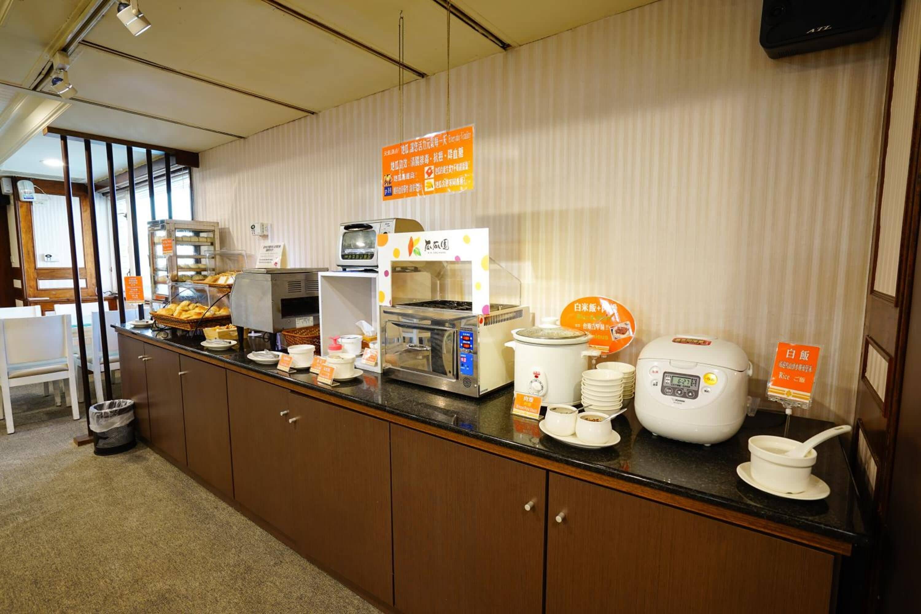 Un'area buffet con diverse postazioni gastronomiche, tra cui una cuociriso, un forno a microonde e un espositore per il pane.