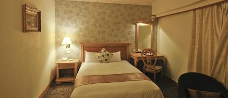 A hotel room with a bed, bedside table, lamp, chair, desk, and a mirror.