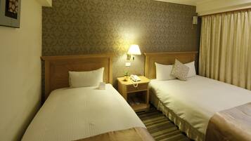Une chambre d’hôtel avec deux lits, une table de chevet avec une lampe et une petite table avec un téléphone et une plante.