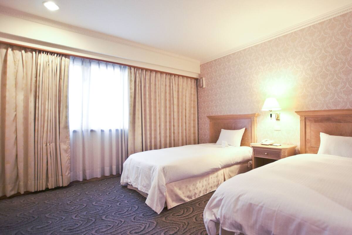 A hotel room with two beds, a nightstand with a lamp, and a patterned carpet.