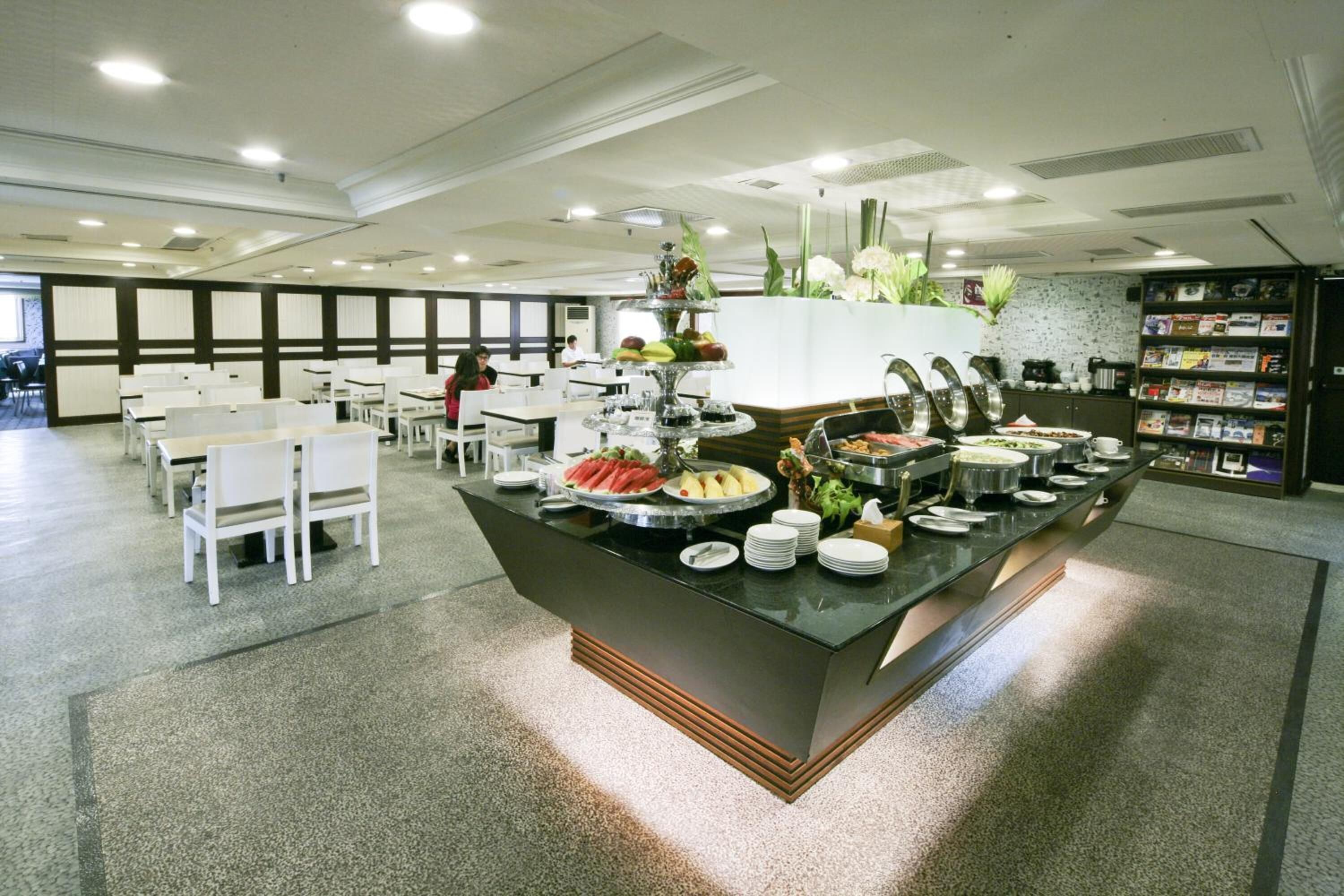 A buffet area with a variety of food options, white tables and chairs, and a decorative plant arrangement.