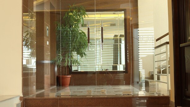 A modern lobby with a glass entrance, a potted plant, and a staircase leading to an upper level. - Garden City Residence (Dekwaneh)