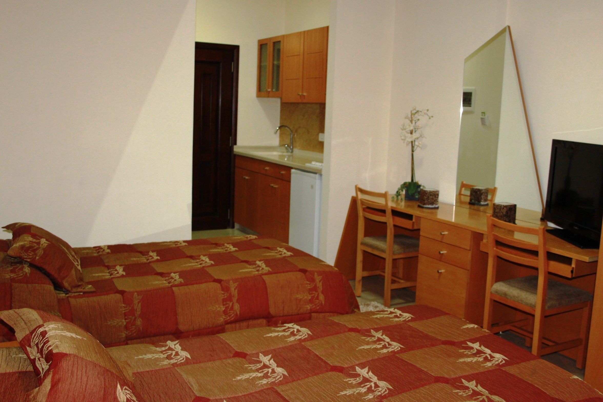 Une chambre compacte comprenant un lit, un bureau, une chaise, un miroir et une petite kitchenette.