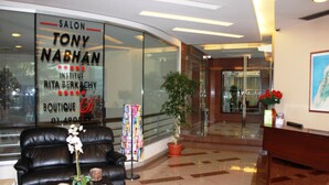 A modern lobby with a leather sofa, a reception desk, and a large window advertising a salon. - Garden City Residence (Dekwaneh)
