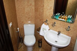 A bathroom with a toilet, sink, and a glass shelf holding toiletries. - Garden City Residence (Dekwaneh)