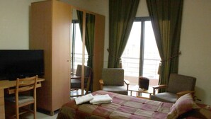 A hotel room with a bed, a TV, a desk, and two chairs. - Garden City Residence (Dekwaneh)