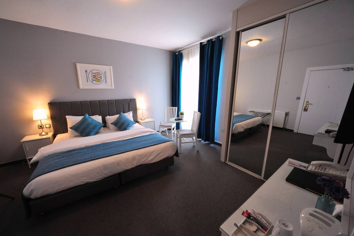 Ein Hotelzimmer mit einem Bett, Nachttisch, Lampe, Stuhl, Schreibtisch und einem Spiegel.