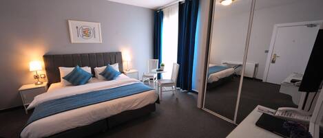 A hotel room with a bed, bedside table, lamp, chair, desk, and a mirror.