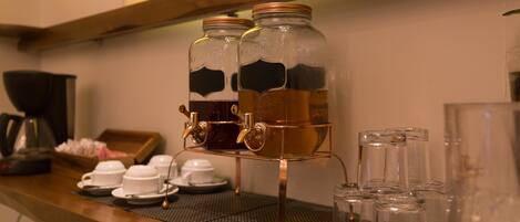A coffee station with two glass dispensers, a coffee pot, and several cups and saucers on a wooden counter.