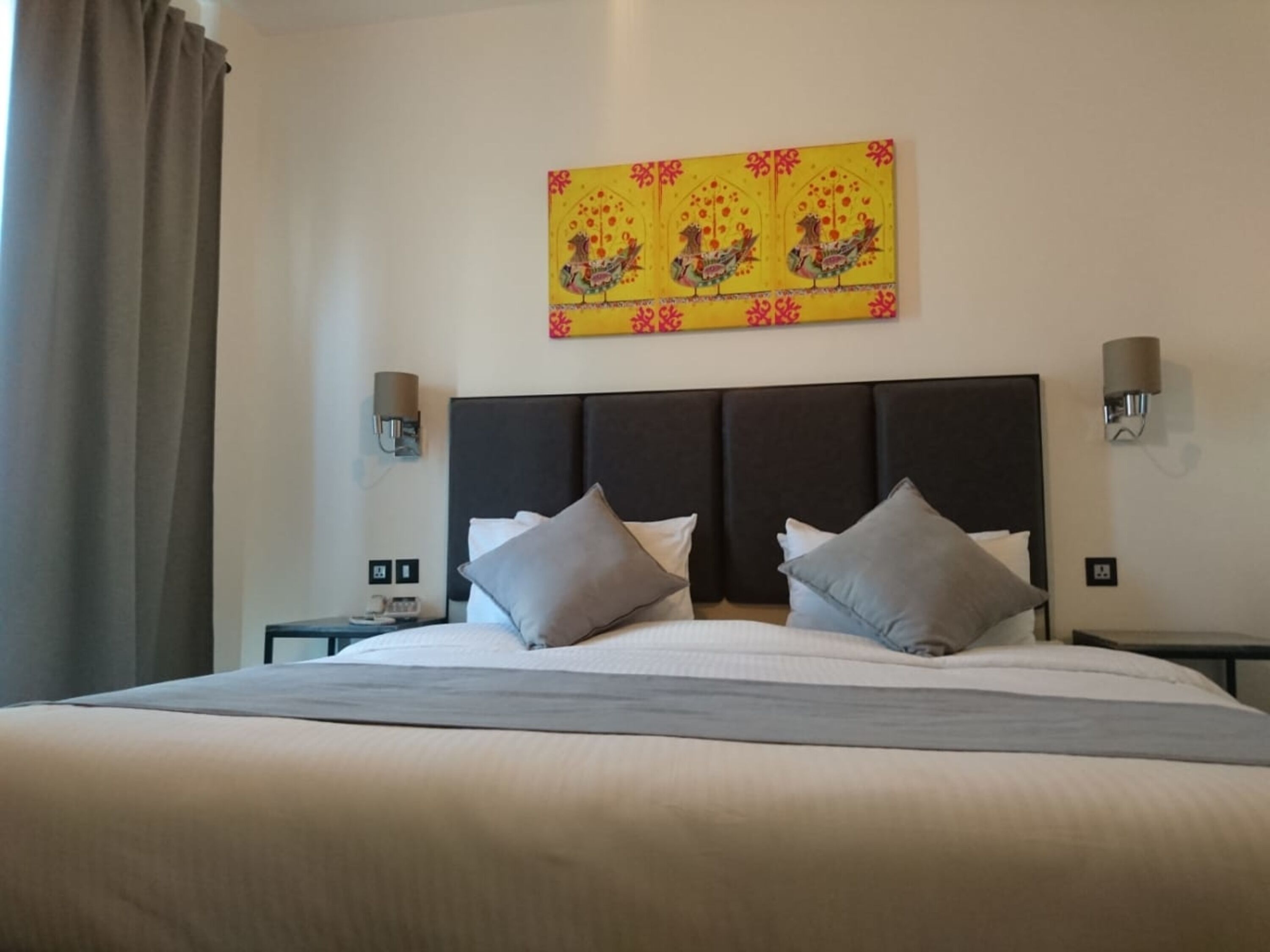Une chambre d’hôtel avec un grand lit, deux tables de chevet, une tête de lit et une œuvre d’art accrochée au mur.