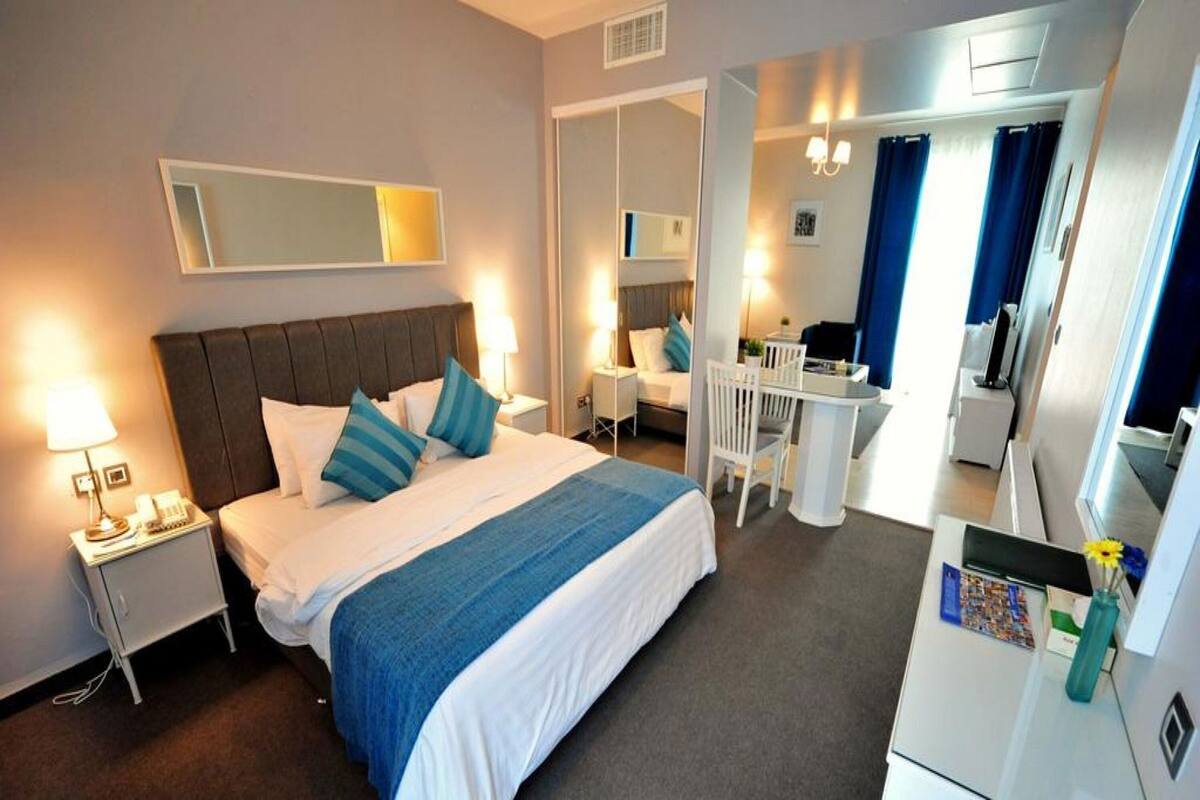 Ein Hotelzimmer mit Bett, Nachttisch, Schreibtisch, Stuhl und einer kleinen Küchenzeile.