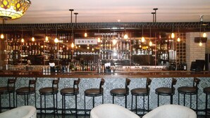 A bar area with a 'DRINK' sign, bar stools, and a variety of bottles and glasses on shelves.