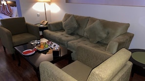 A cozy living area with a sofa, armchairs, a coffee table with fruits and snacks, a lamp, and a telephone.