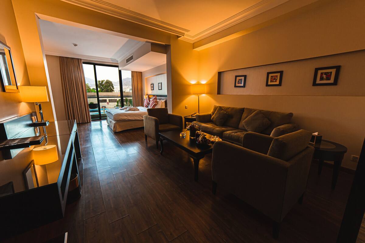 A hotel room with a living area, a bed, a desk, and a balcony with a view.