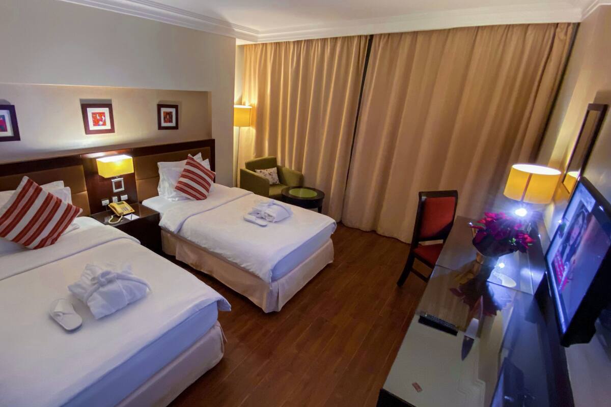 A hotel room with two beds, a desk with a computer, a chair, and a TV.