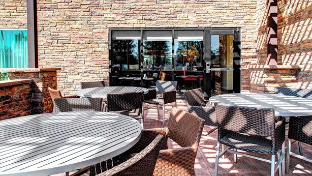 An outdoor patio with wicker furniture, a brick wall, and a glass door leading to the interior. - Towneplace Suites Bakersfield West (Bakersfield)