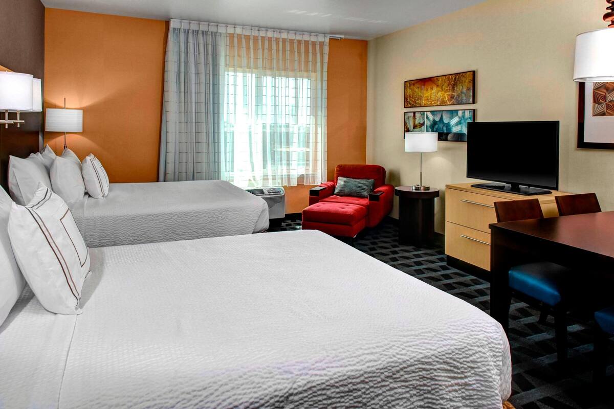 Habitación de hotel con dos camas, televisión, escritorio y una silla.