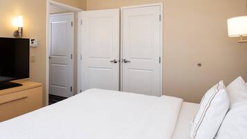 A hotel room with a bed, a TV, a desk, and two doors.