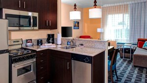 A compact kitchen with a microwave, stove, and dishwasher, a dining area with a table and chairs, and a living room with a sofa and a TV. - Towneplace Suites Bakersfield West (Bakersfield)