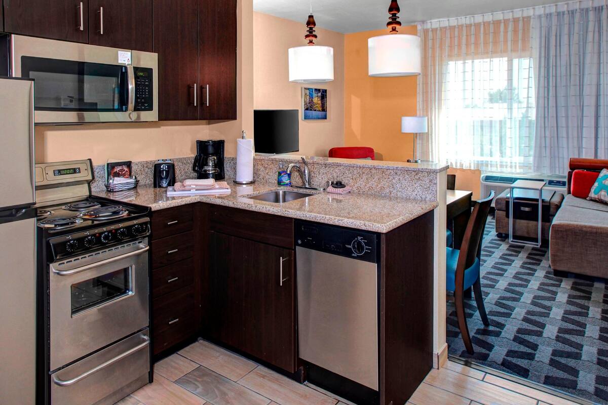 Una cocina compacta equipada con microondas, estufa y lavavajillas, un comedor con mesa y sillas, y una sala de estar con sofá y televisor.
