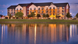 A multi-story hotel with a reflective pool in front, featuring a modern architectural design with a mix of beige and brown colors. - Towneplace Suites Salt Lake City-West Valley (West Valley City)