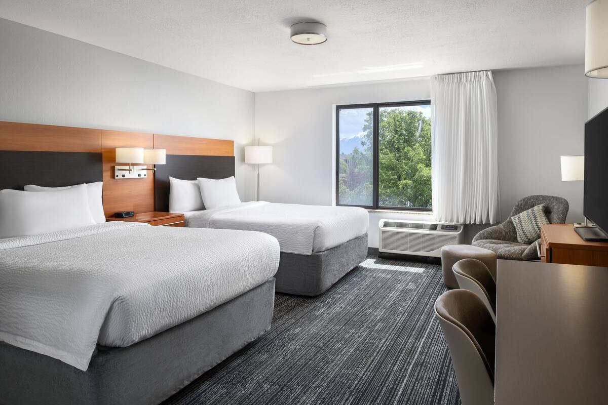 Une chambre d’hôtel avec deux lits, un bureau, une chaise, une télévision et une fenêtre avec des rideaux.