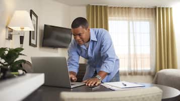 A hotel room with a desk, laptop, and a television on the wall.