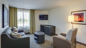 A hotel room with a sofa, armchair, small table, and a TV on the wall.
