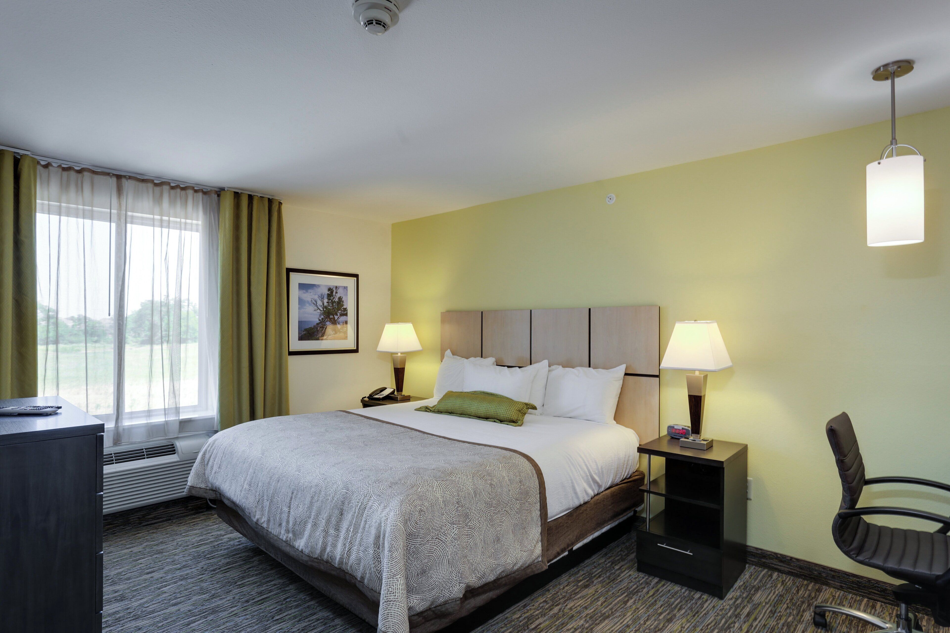 A hotel room with a bed, bedside lamps, a desk, and a chair.