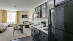 Una habitación de hotel moderna con cama, zona de comedor, cocina con refrigerador y baño.