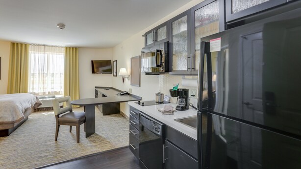 A modern hotel room with a bed, a dining area, a kitchen with a refrigerator, and a bathroom.