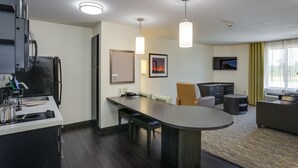 A modern hotel room with a kitchenette, a dining area, and a living space.