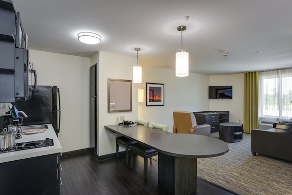 A modern hotel room with a kitchenette, a dining area, and a living space.