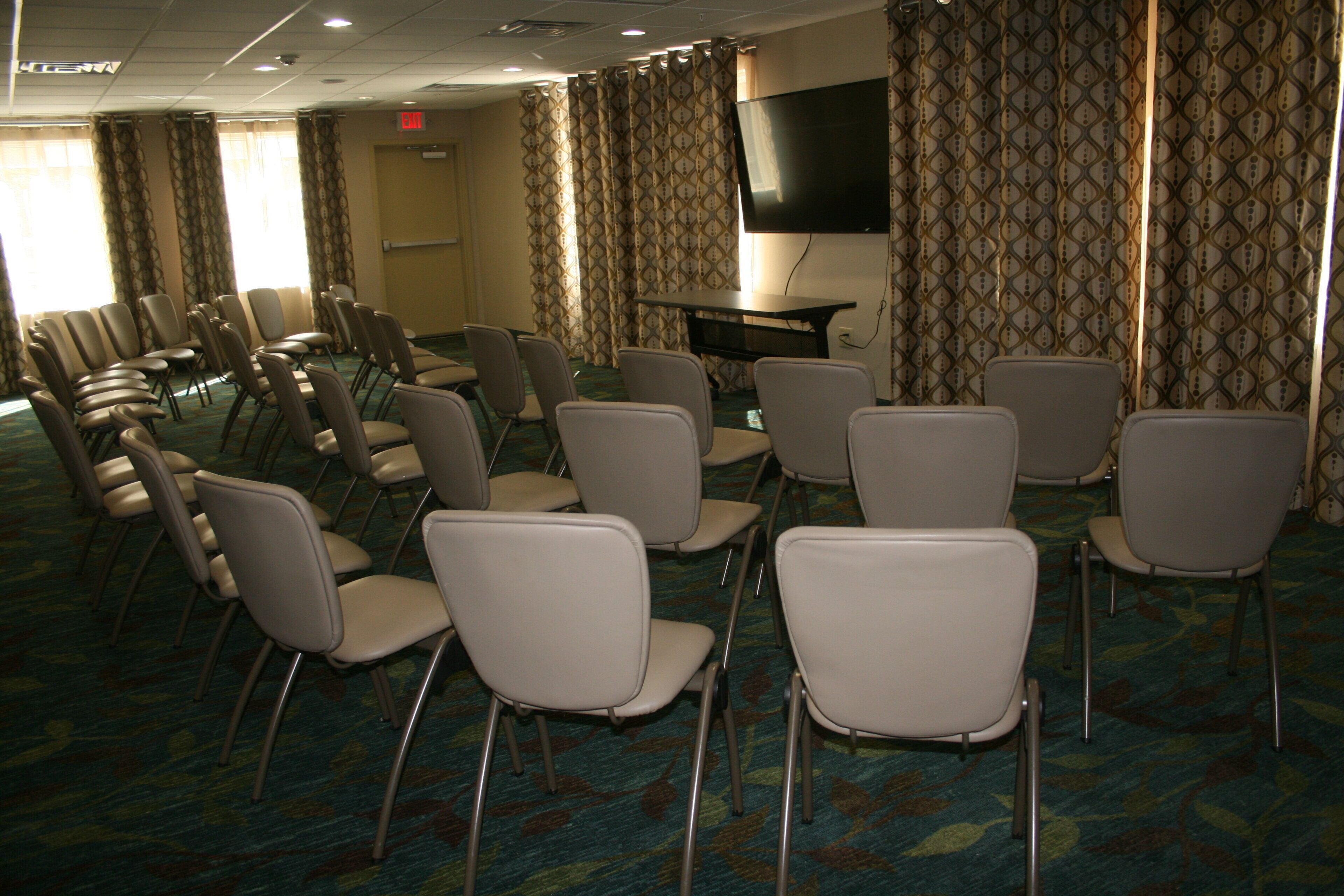 Une salle de conférence avec des rangées de chaises, une table et un écran de t élévision.