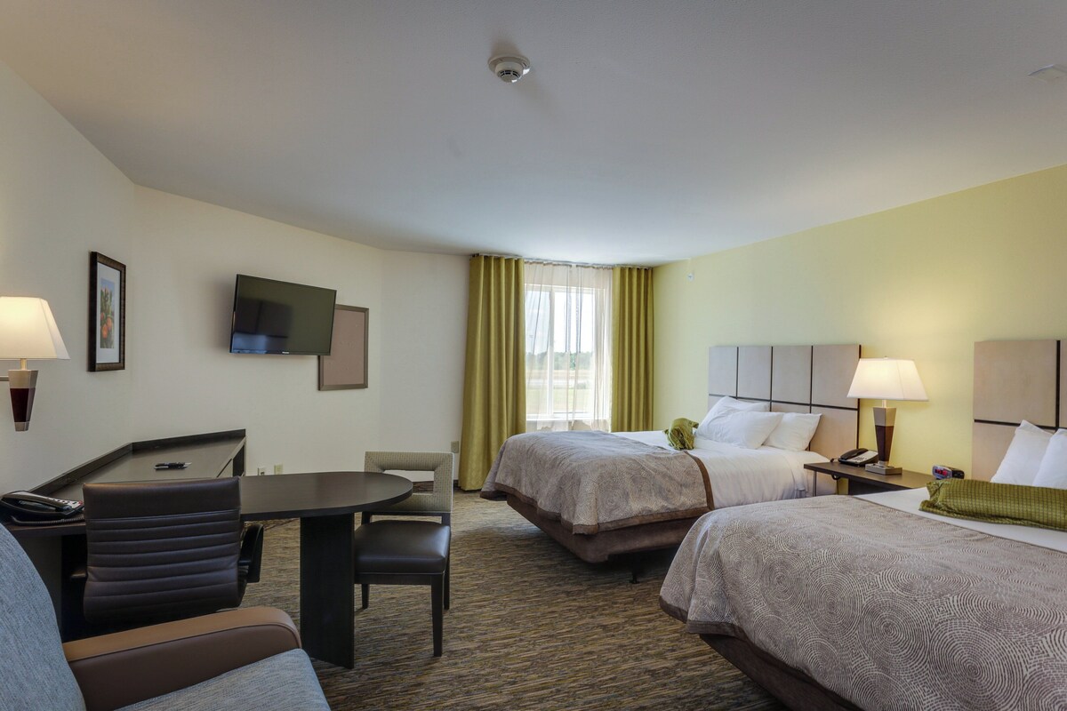 A hotel room with a desk, two beds, a TV, and a window with curtains.