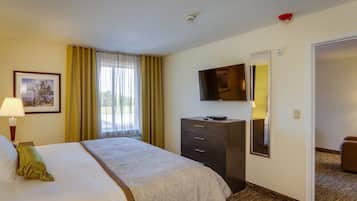 A hotel room with a bed, a dresser, a television mounted on the wall, and a door leading to another room.