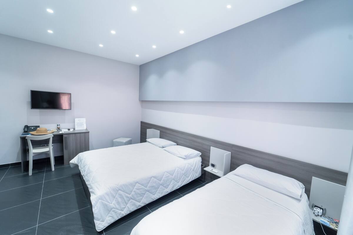 Une chambre d’hôtel moderne équipée de deux lits, d’un bureau, d’une télévision à écran plat et d’une table de chevet avec une lampe.