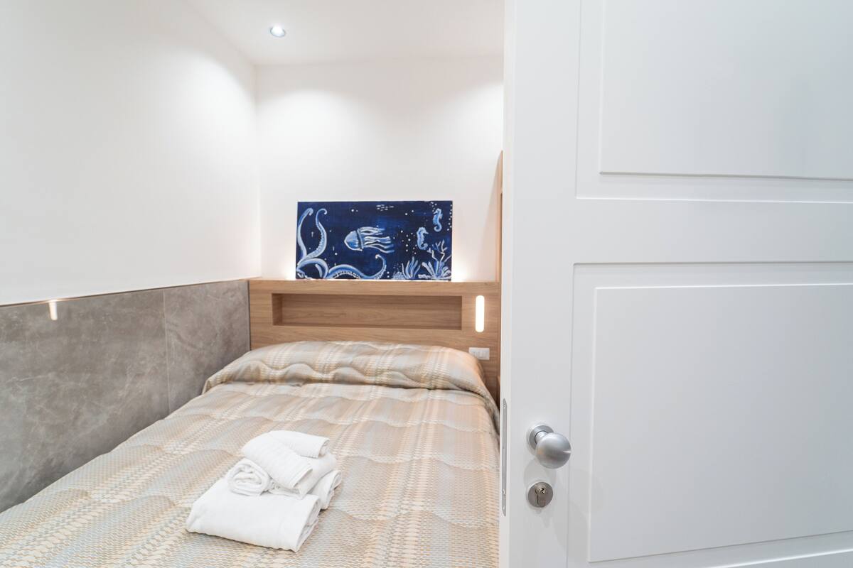 Un lit bien fait, avec une couvre-lit à motifs et des serviettes pliées, une tête de lit en bois et une œuvre d’art accrochée au mur représentant la vie aquatique.