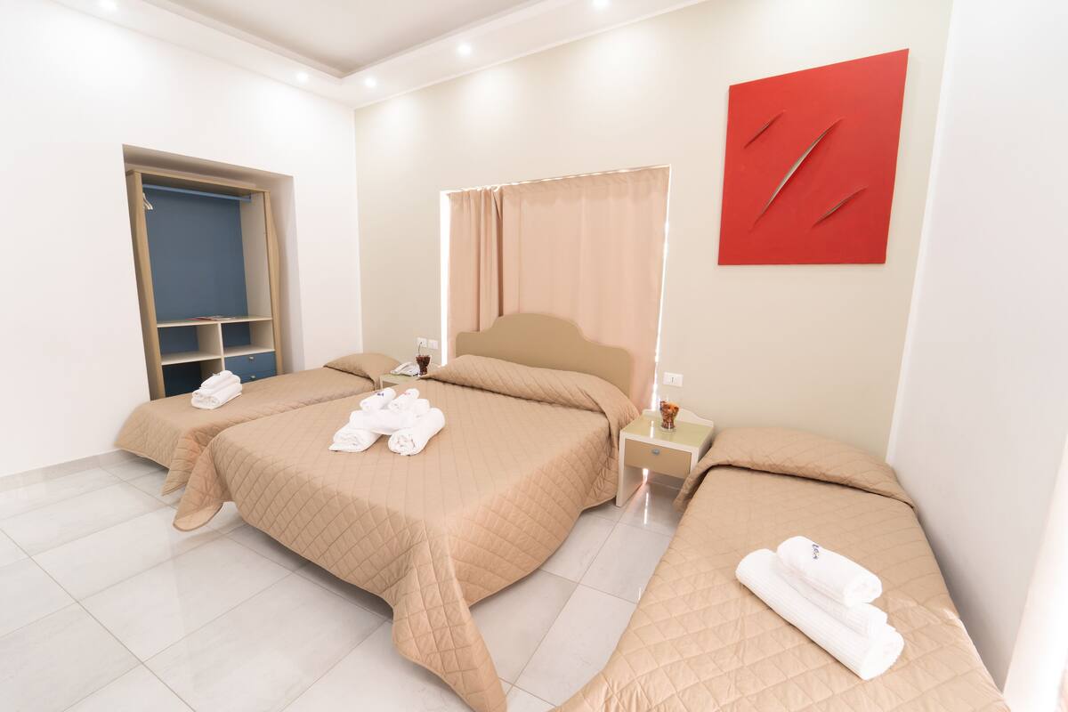 Une chambre d’hôtel avec deux lits, une armoire, une table de chevet et une œuvre d’art rouge accrochée au mur.