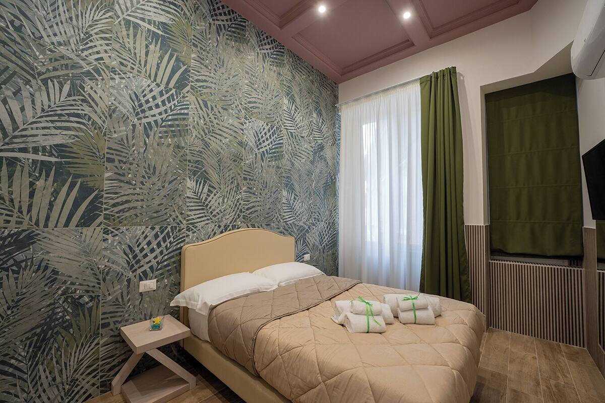 Une chambre à coucher avec un lit, une table de chevet, une fenêtre avec des rideaux et un radiateur.
