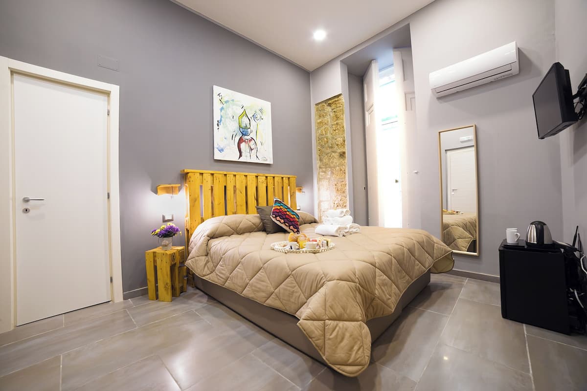Une chambre moderne avec un grand lit, une table de chevet avec une lampe, un miroir et un appareil de climatisation.