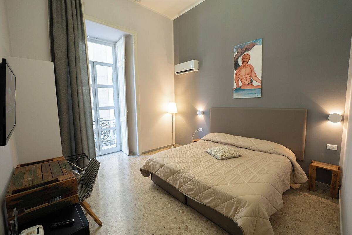 Une chambre à coucher avec un lit, des lampes de chevet, un tableau et une vue sur l’extérieur, visible à travers une porte ouverte.