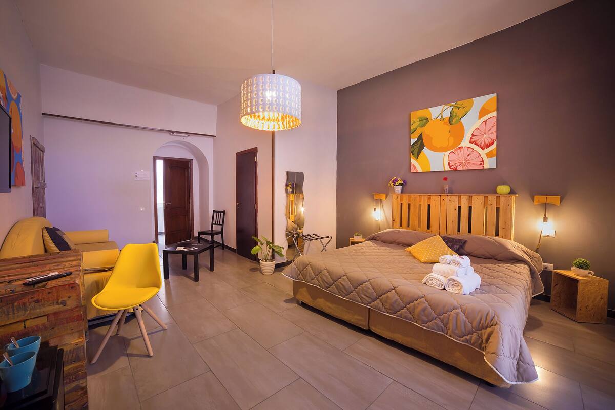 Une chambre moderne avec un grand lit, une chaise jaune, un bureau et un coin repas.