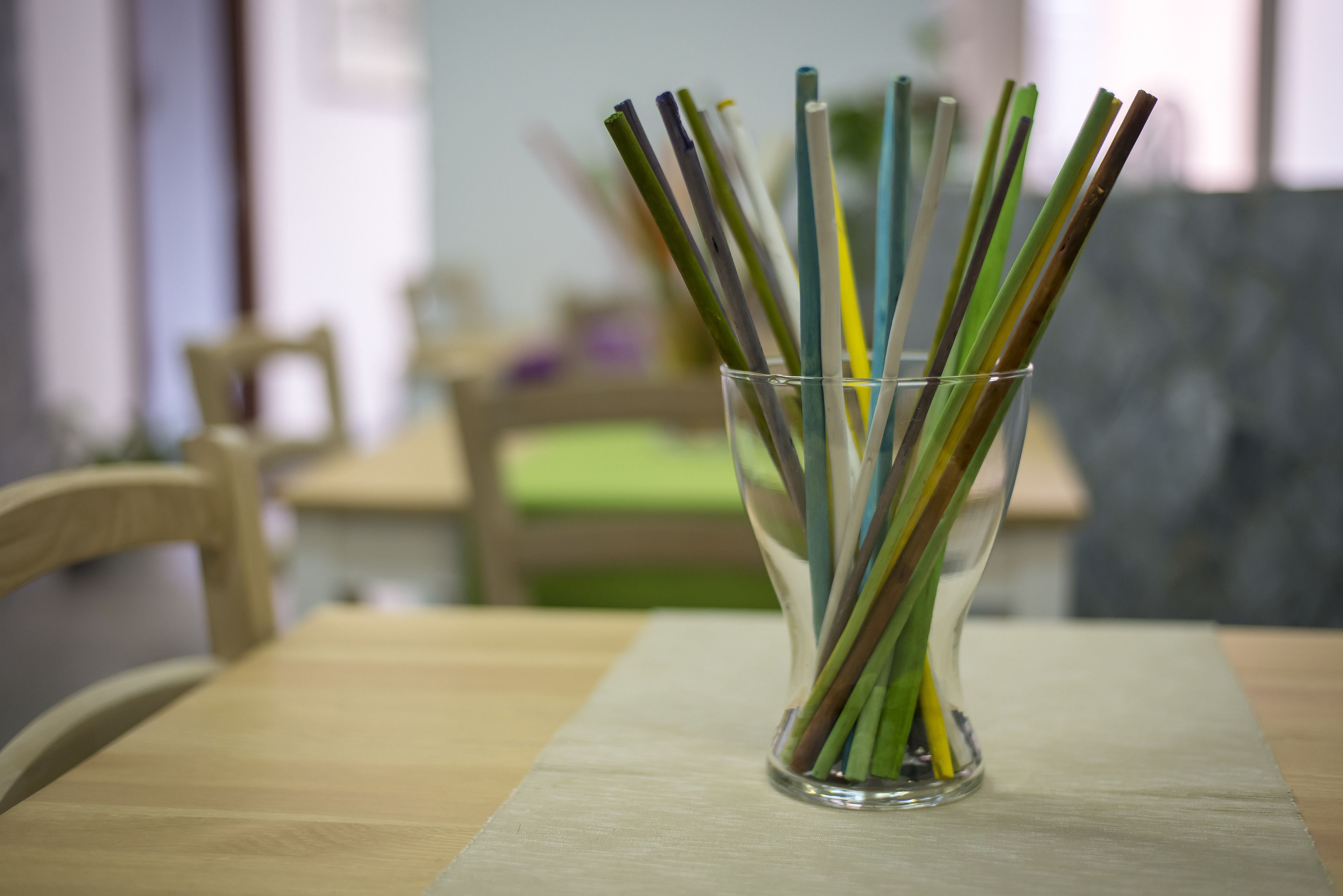 Un florero de vidrio transparente con pajitas de colores sobre una mesa de madera.