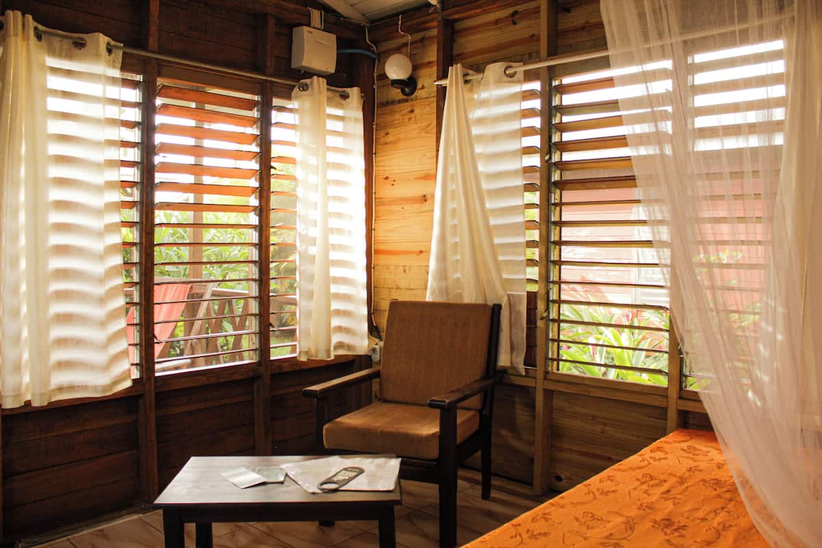 A wooden room with a single chair, a table with a remote control, and a bed with a floral bedspread.