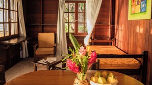 Una habitación de madera con una cama, una silla, una mesa con un jarrón de flores y una ventana con cortinas.