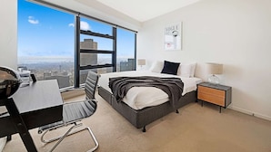 A modern hotel room with a large window offering a city view, a bed with a black and white striped blanket, a bedside table with a lamp, and a desk with a chair. - Southbank Apartments - Eureka Tower (Southbank)