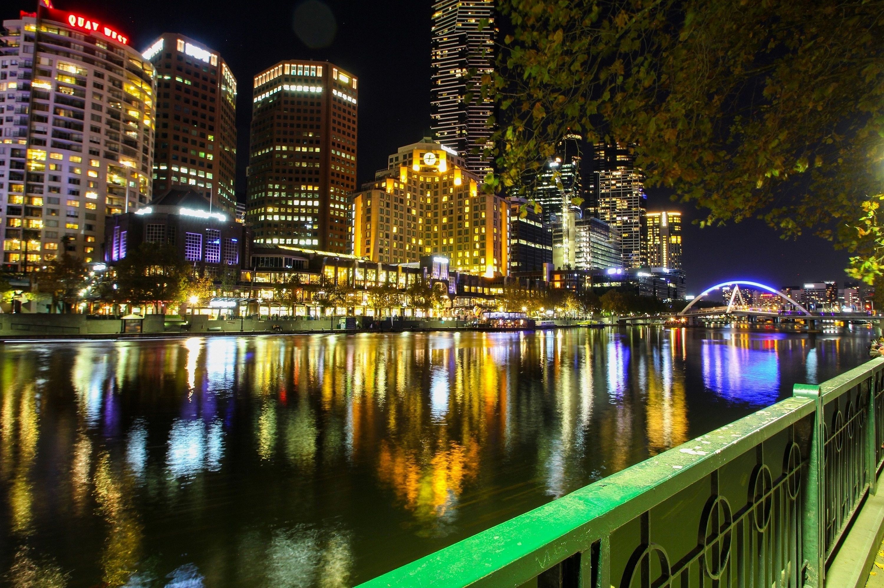 A nighttime cityscape with illuminated buildings reflecting on a calm river.
